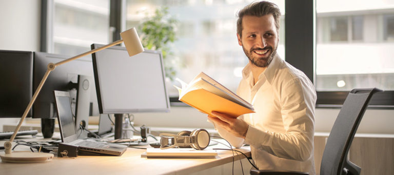 Klinische Prüfungen im Rahmen der MDR/IVDR. Ein Geschäftsmann sitzt an einen Schreibtisch und hält ein Buch in den Händen.